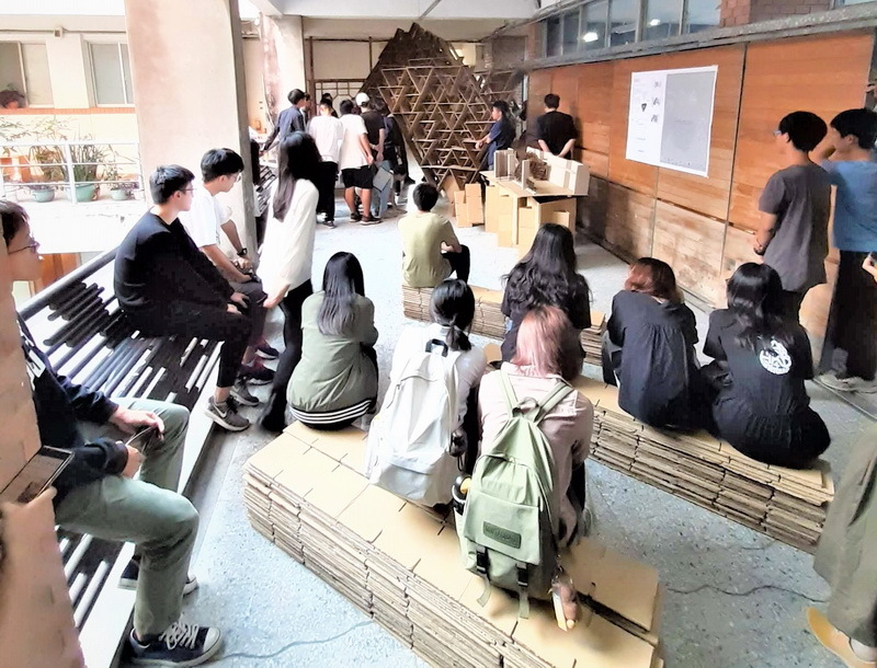學生們坐在自己搭建的紙構築進行評圖