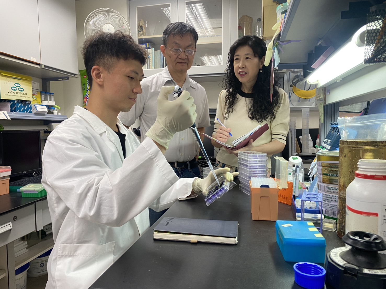 圖五：成大藥理學研究所所長王憶卿講座教授（右）與生物科技與產業科學系洪建中特聘教授（中）與博士生謝宏嘉在實驗室中的情況。